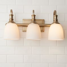 three light bathroom fixture with white glass shades on the wall and brick tile backsplash