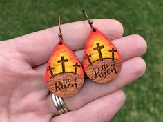 a pair of wooden earrings with crosses and the words, he is risen on them