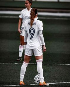 two female soccer players are standing on the field together and one is holding a ball