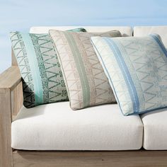 four pillows are sitting on top of a white couch in front of the ocean and blue sky