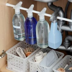 three bottles of cleaning products are sitting in the under - cabinet drawer organizer, which is organized with plastic baskets