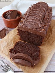 a chocolate cake with frosting and sprinkles next to a fork on a piece of parchment paper