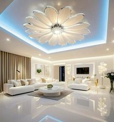 a large living room with white furniture and lights on the ceiling, along with flowers in vases