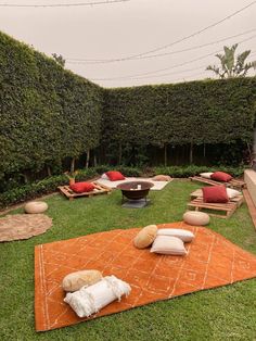 an outdoor seating area with cushions and pillows on the grass in front of a hedge