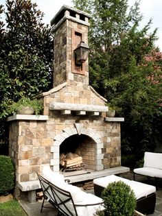 an outdoor fireplace in the middle of a patio with furniture around it and trees behind it