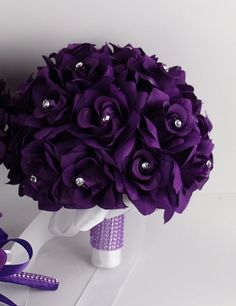 a bouquet of purple flowers is sitting on top of a white vase with ribbon and jeweled decorations