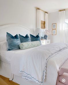 a white bed with four pillows on top of it in a bedroom next to a window