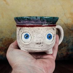 a hand holding a ceramic cup with eyes on it