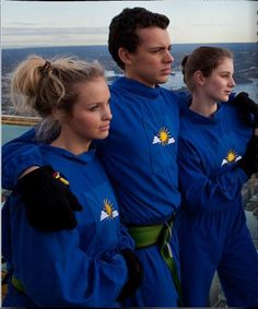 three people dressed in blue standing next to each other on a boat looking out at the water