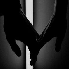 two hands holding each other in the shape of a heart on a dark room wall