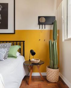 a bedroom with yellow walls and a cactus on the table in front of the bed