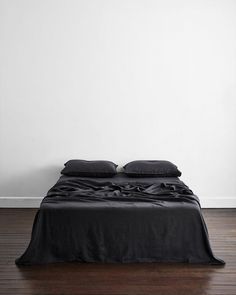 a bed with black sheets and pillows on top of it in front of a white wall