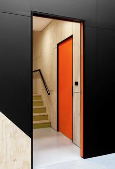 an orange door is open in front of a black wall and stairs with wood paneling