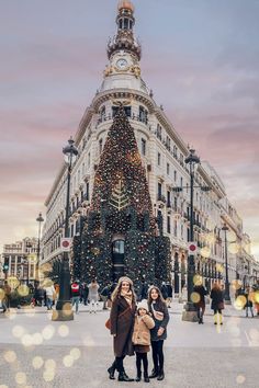 two women standing in front of a building with a christmas tree on the corner and lights all around