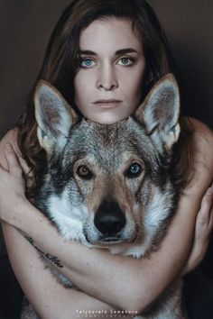 a woman is hugging a wolf with her arms around her head and looking at the camera