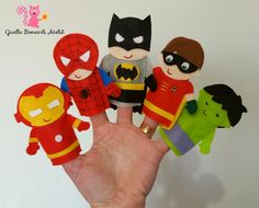 a hand is holding up several small felt superheros and spider - man dolls in different colors