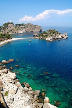 the water is crystal blue and clear with rocks on both sides, and small islands in the distance