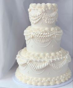 a three tiered white wedding cake with ruffles on the bottom and sides