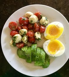 a white plate topped with eggs, tomatoes and cucumber on top of a table