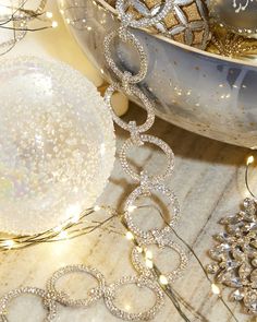 silver and white ornaments are sitting on a table next to a bowl full of christmas balls