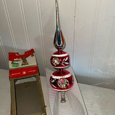 a red and silver christmas ornament sitting on top of a glass table next to a box