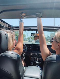 two women sitting in the driver's seat of a car with their hands up