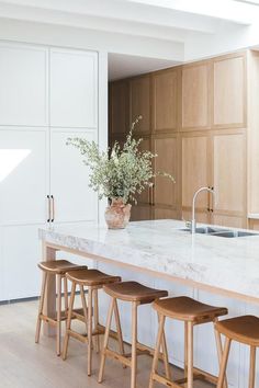 a kitchen island with four stools and a sink in the center is surrounded by wooden cabinets