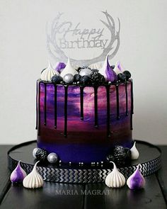 a purple and black cake with white frosting on top is sitting on a table