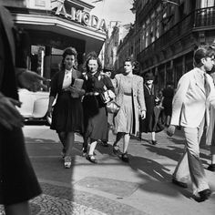 black and white photograph of people walking down the street in front of a movie theater