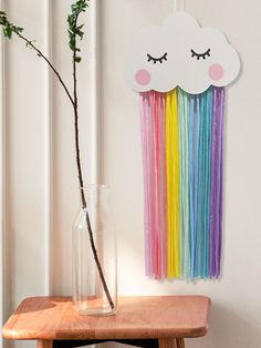 a vase filled with flowers next to a rainbow wall decoration on a wooden table in front of a white wall