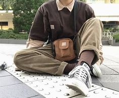 a man sitting on the ground with his legs crossed, wearing brown pants and white sneakers