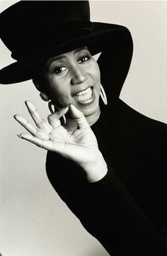 a black and white photo of a woman wearing a hat with her hands in the air