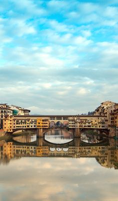 a bridge over a body of water with buildings on both sides and clouds in the sky