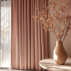 a vase filled with flowers sitting on top of a table next to a window covered in pink curtains