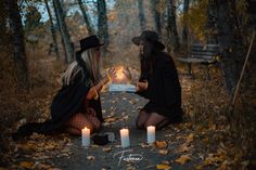 two women sitting on the ground with candles in their hands and one holding a book