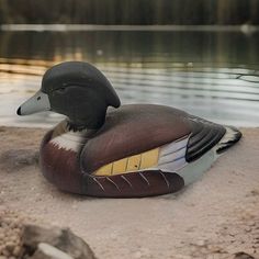 a duck is sitting on the sand by the water with its head turned to the side