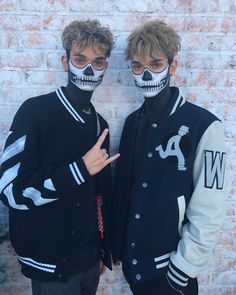 two young men with painted faces standing next to each other in front of a brick wall