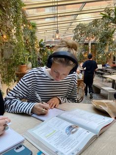 a woman sitting at a table writing in a book with headphones on her head