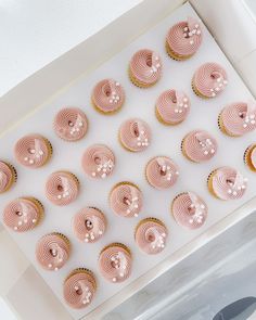 cupcakes with pink frosting are arranged in a square box on a table