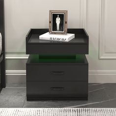 a black table with two drawers and a framed photo on top, in front of a white wall