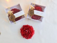 two small boxes with red roses in them on a white tablecloth and gold accents