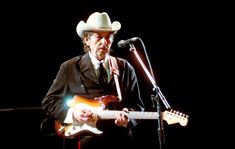 a man wearing a cowboy hat and holding a guitar while standing in front of a microphone