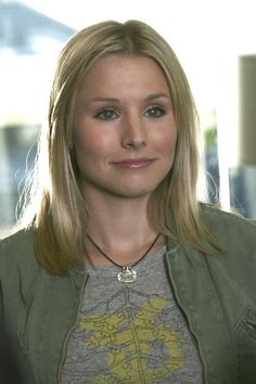 a woman with blonde hair wearing a green jacket and gray t - shirt is looking at the camera