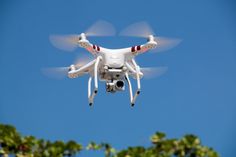 a white quadcopter flying through the air with trees in the foreground