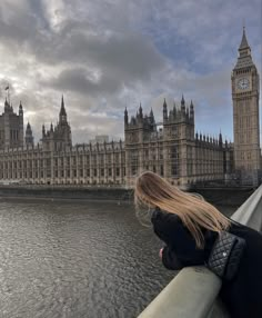 a woman is looking out over the water in front of big ben and the houses of parliament