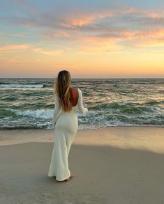 a woman standing on top of a sandy beach next to the ocean at sun set