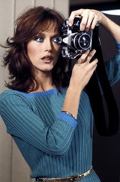 a woman holding up a camera in front of her face and wearing a blue dress