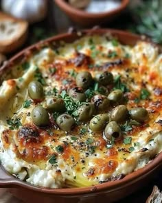 a bowl filled with cheese and olives on top of a table next to bread