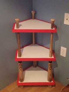 a red and white three tiered shelf with wood handles on each side in the corner