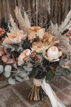 a bouquet of flowers sitting on top of a brick floor next to a wooden fence